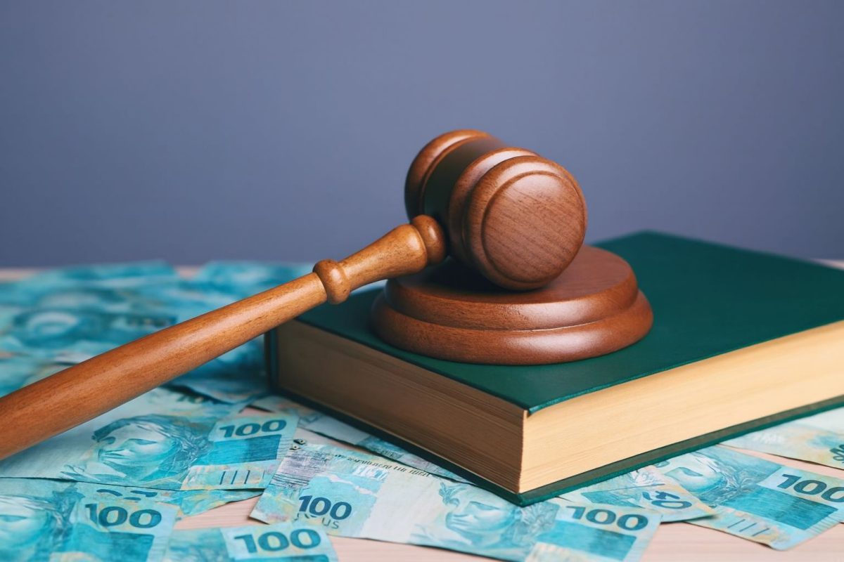 Elemento gráfico - martelo jurídico sobre livro que lembra a constituição, sobre notas de 100 reais